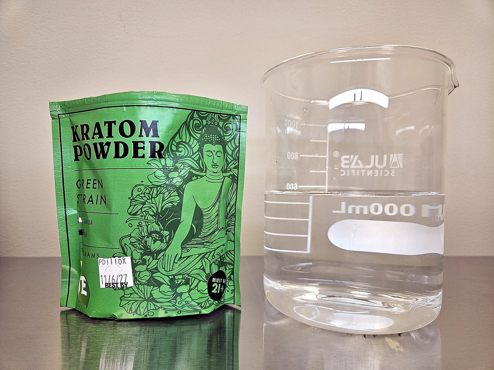 Clear glass of water beside a sealed green kratom powder pouch, before mixing.